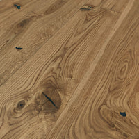 Rustikales Eiche-Parkett mit lebendiger Maserung, natürlichen Ästen und schwarz gespachtelten Rissen in warmem Holzfarbton.