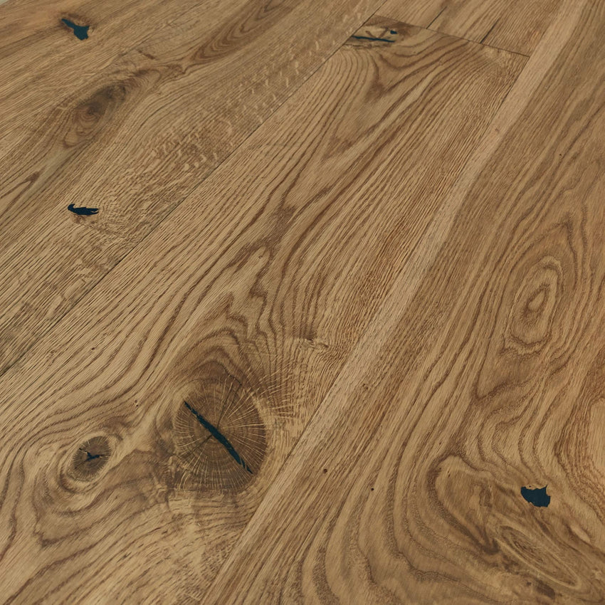 Rustikales Eiche-Parkett mit lebendiger Maserung, natürlichen Ästen und schwarz gespachtelten Rissen in warmem Holzfarbton.