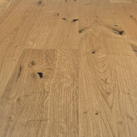 Rustikales Eiche-Parkett mit lebendiger Maserung, natürlichen Ästen und schwarz gespachtelten Rissen in warmem Holzfarbton.