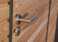 Detailaufnahme einer Edelstahl-Drückergarnitur mit Schloss an der horizontalen Rhombusschalung eines modernen Holz-Gartenhauses
