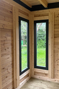 Innenansicht eines modernen Holz-Gartenhauses mit vertikalen Fenstern mit dunklen Rahmen aus Lärchenholz