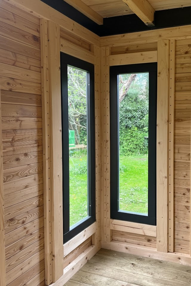 Innenansicht eines modernen Holz-Gartenhauses mit vertikalen Fenstern mit dunklen Rahmen aus Lärchenholz