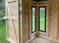 Innenansicht eines modernen Holz-Gartenhauses mit geöffneter Tür, zwei vertikalen Fenstern mit dunklen Rahmen aus Lärchenholz