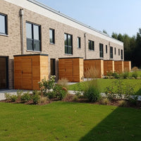 Mehrere moderne Gartenschränke aus Lärchenholz mit Rhombusfassadenprofil in einer gepflegten Wohnanlage mit Grünflächen und Blumenbeeten.