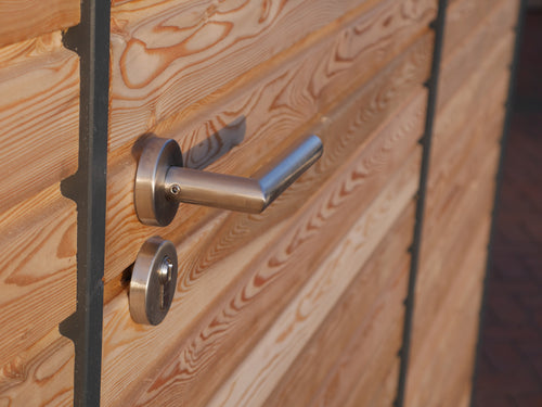 Edelstahldrückergarnitur an Tür mit waagerechter Rhombusschalung aus Holz für das Gartenhaus KLARE LINIE